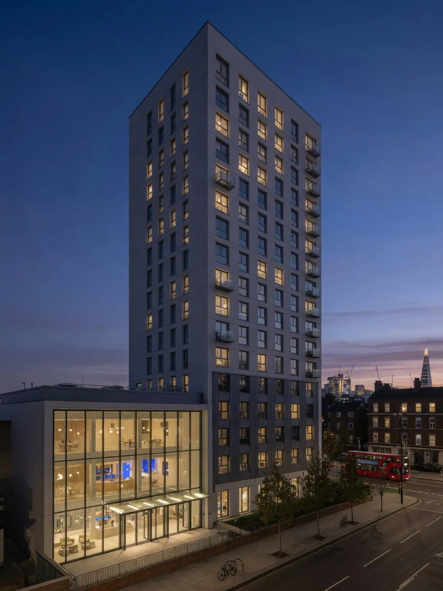 Modern residential tower at dusk with lit windows against a deep blue sky
