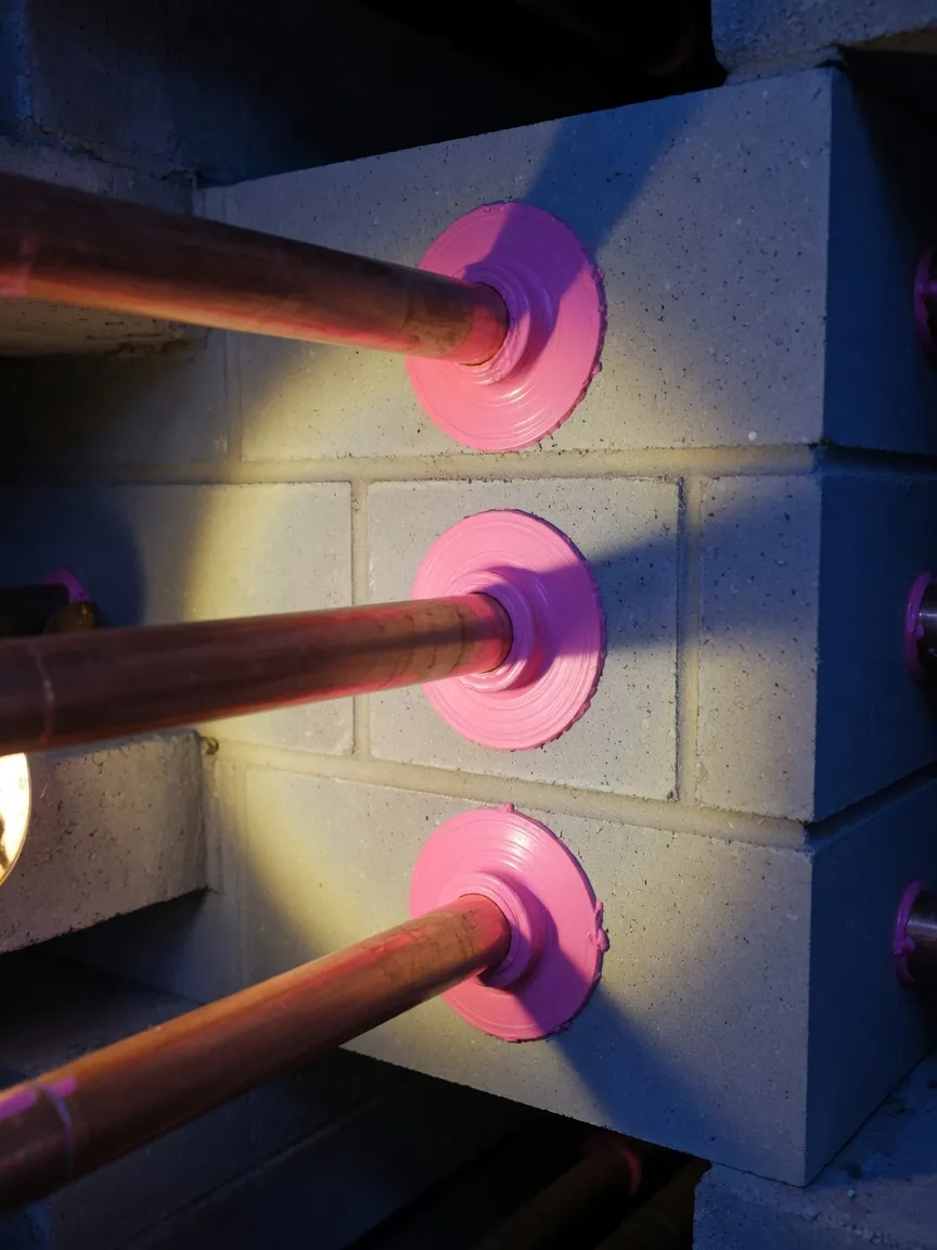Neatly sealed pipe penetrations through a blockwork wall in torchlight
