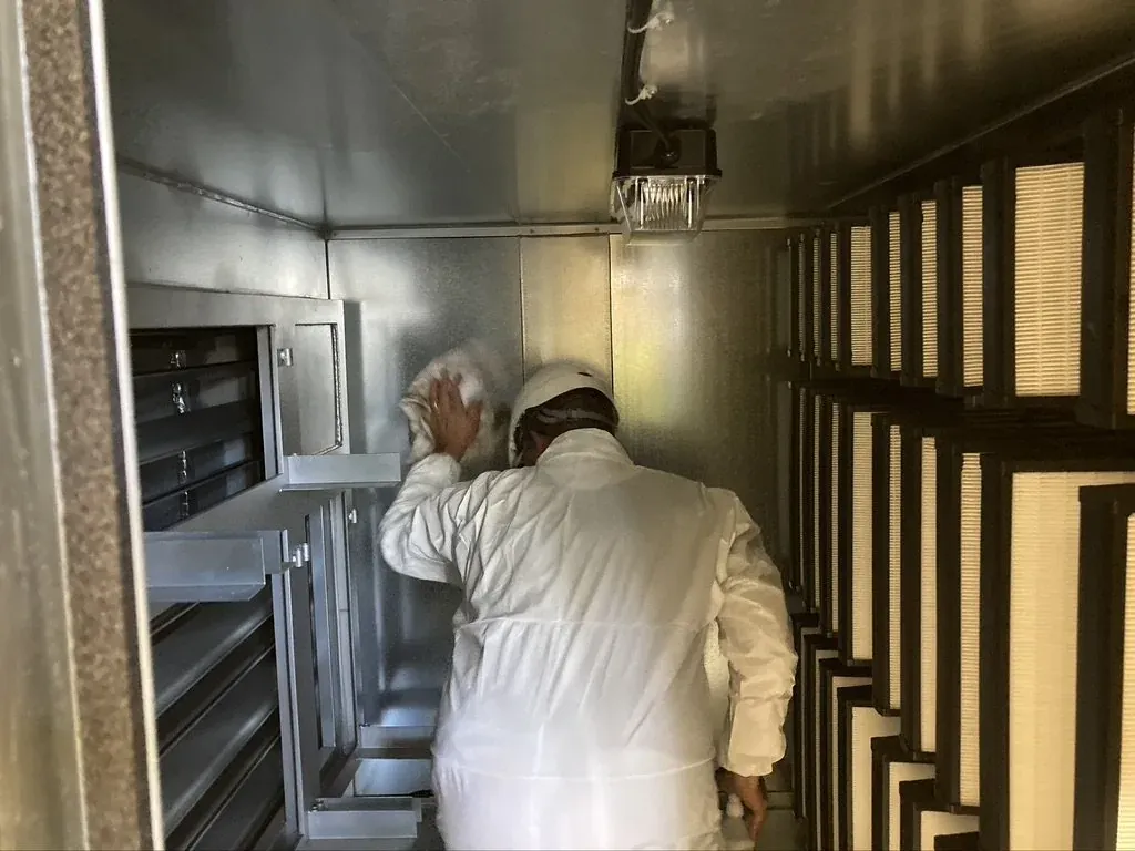 Technician cleaning inside an air handling unit beside its filter banks